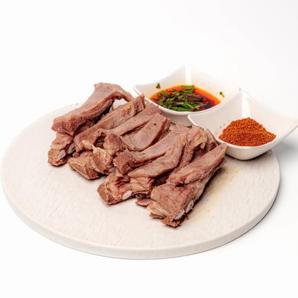Halal lamb ribs, sliced and served with chili oil and a bowl of red spice on a white plate.