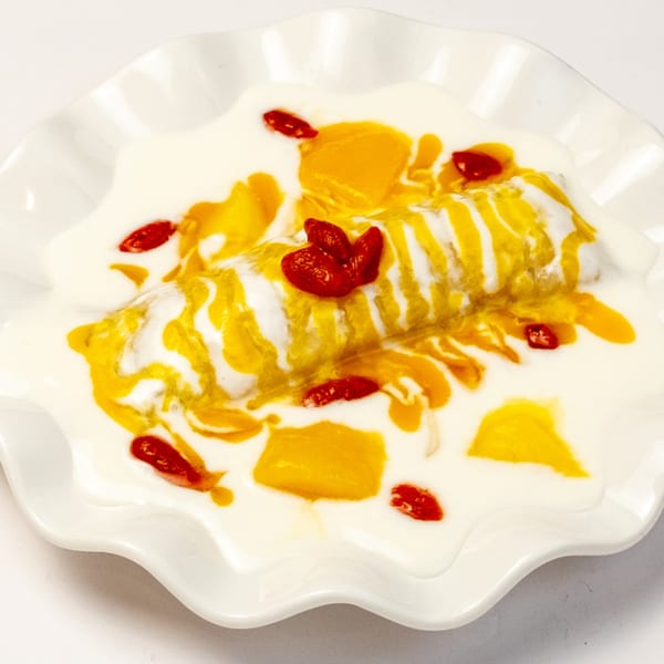 Halal mango dessert with cream, mango chunks, and red berries on a white ruffled plate.