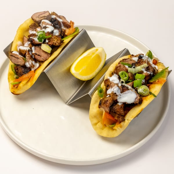 Two halal tacos with meat, white sauce, and green onions, served with a lemon wedge.