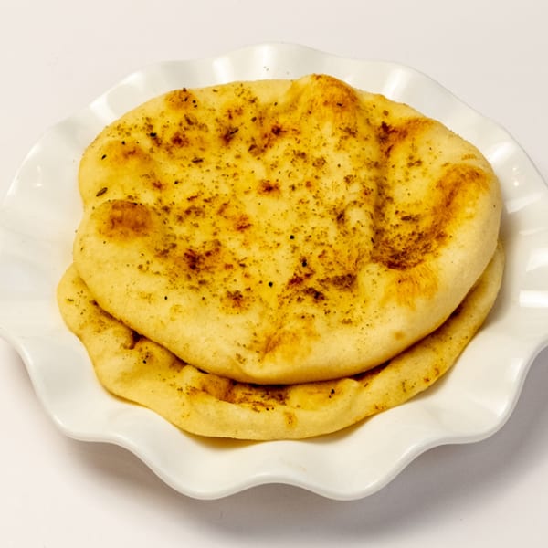 Two pieces of golden-brown naan bread, sprinkled with herbs, on a white ruffled plate.