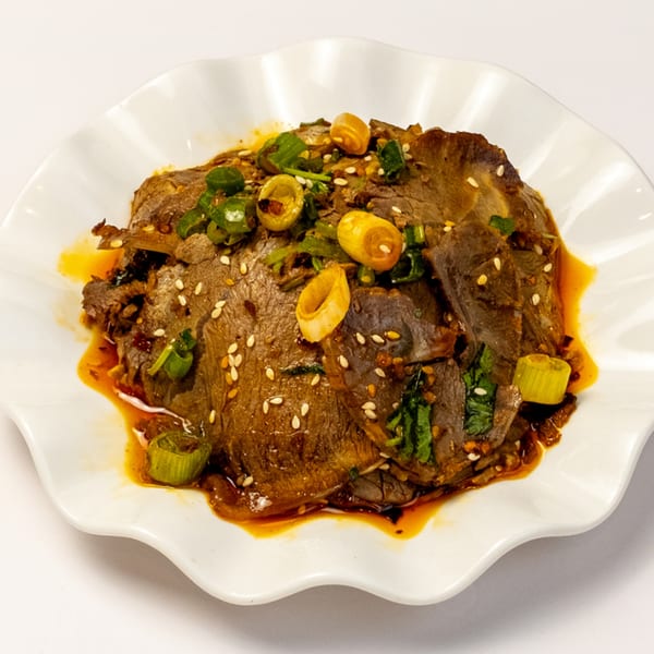 Halal beef slices with sesame seeds, green onions, and chili oil on a white scalloped plate.