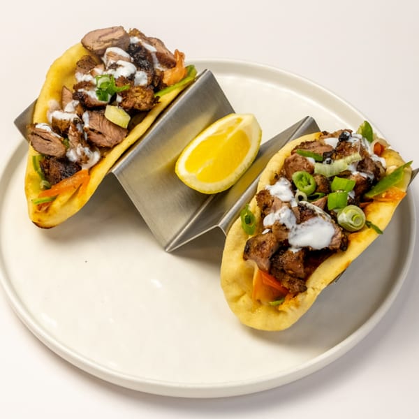 Two Kusan Collective halal tacos with meat, sauce, and green onions, served with a lemon wedge.