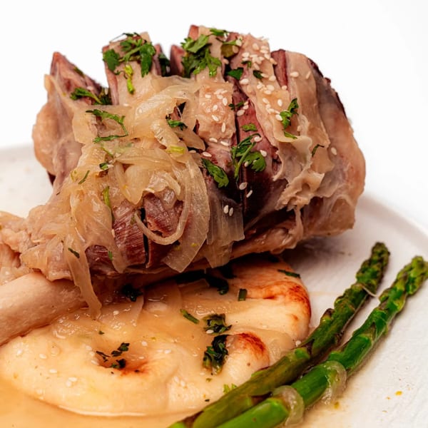 Halal lamb shank with caramelized onions, sesame seeds, and parsley, served with naan and asparagus.
