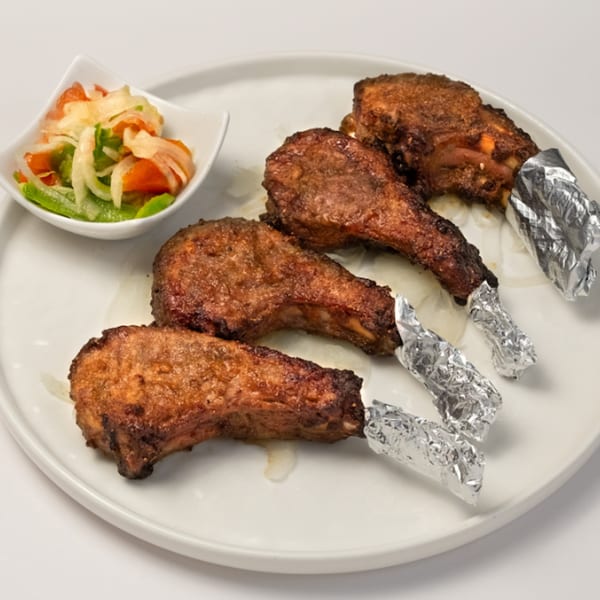 Four Kusan Collective halal lamb chops with foil-wrapped bones and a side of salad.