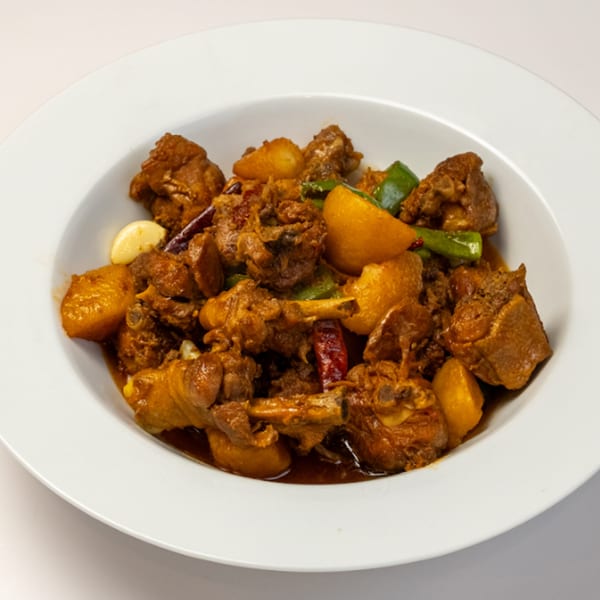 Halal chicken and potato stew with green peppers, garlic, and red chilies in a white bowl.