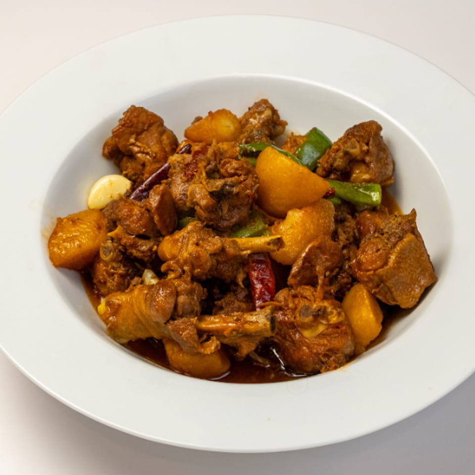Halal chicken and potato stew with green peppers, garlic, and red chilies in a white bowl.