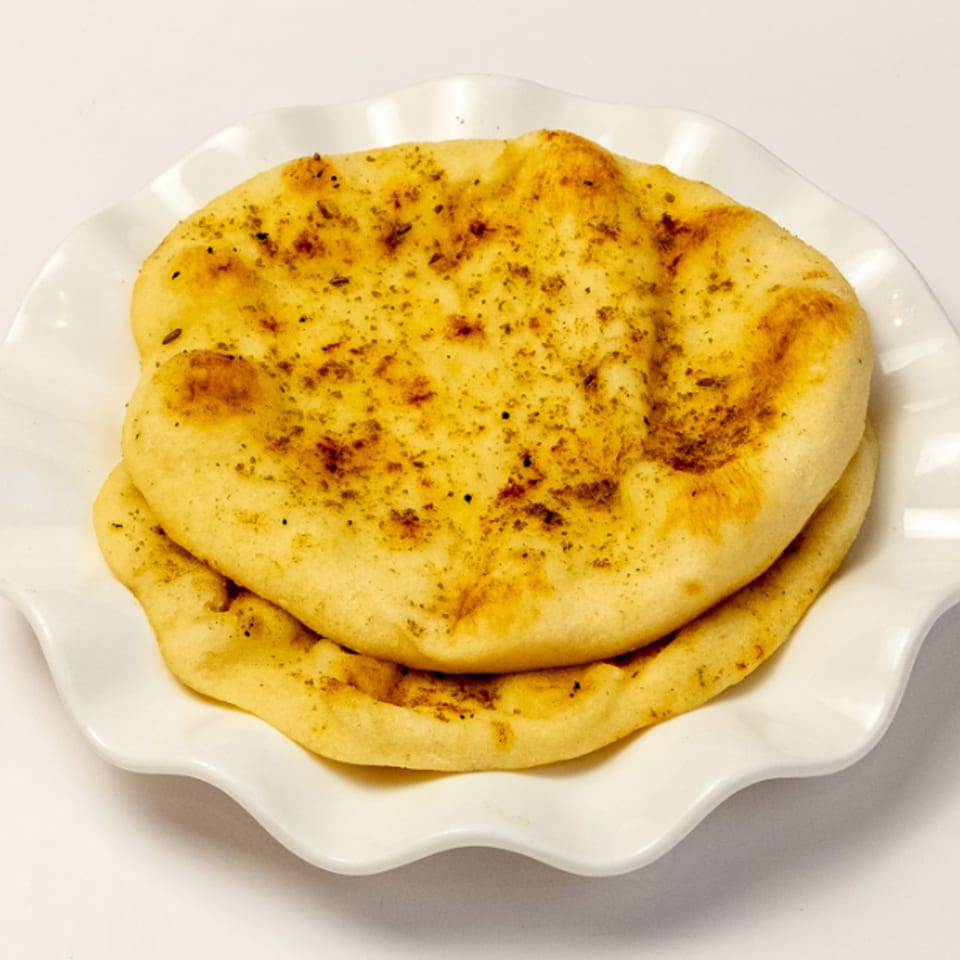 Two pieces of golden-brown naan bread, lightly seasoned, stacked on a white ruffled plate.