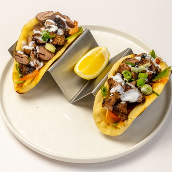 Two Kusan Collective halal tacos with meat, sauce, and green onions, served with a lemon wedge.