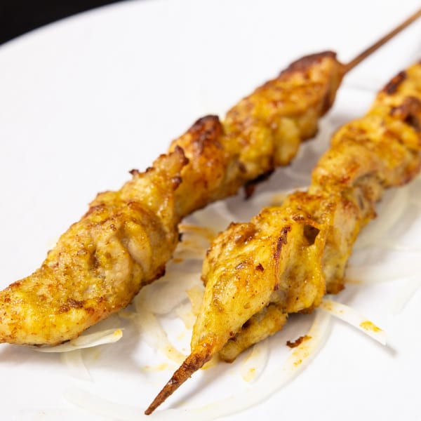 Two golden-brown chicken skewers, likely halal, resting on a bed of thinly sliced white onions.