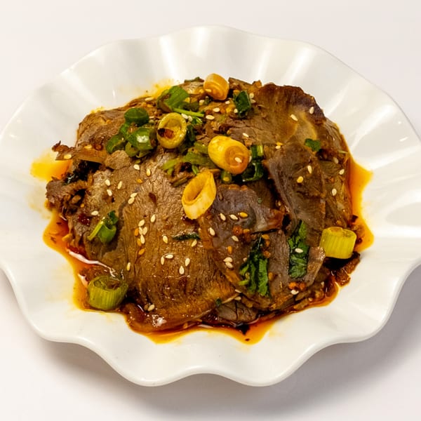 Halal beef slices with sesame seeds, green onions, and chili oil on a white scalloped plate.