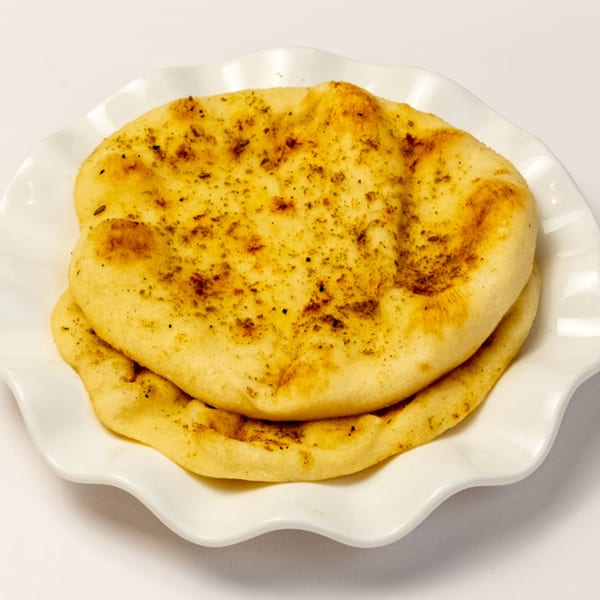 Two pieces of golden-brown Kusan Collective naan bread, sprinkled with herbs, on a white ruffled plate.