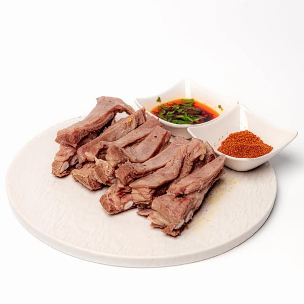 Halal lamb ribs on a white plate with two small bowls of dipping sauce and chili powder.