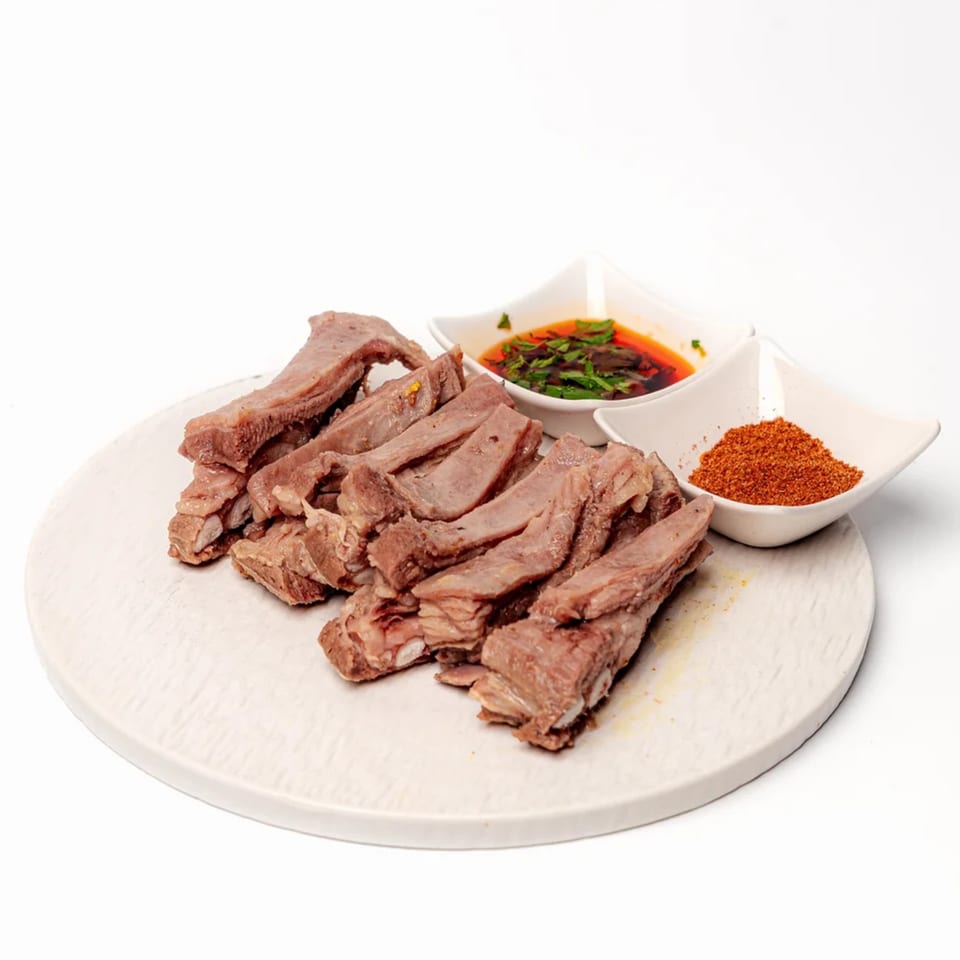 Halal sliced lamb ribs with chili oil and red spice powder on a white plate.