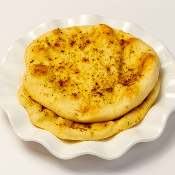 Two pieces of golden-brown naan bread, lightly seasoned, stacked on a white ruffled plate.
