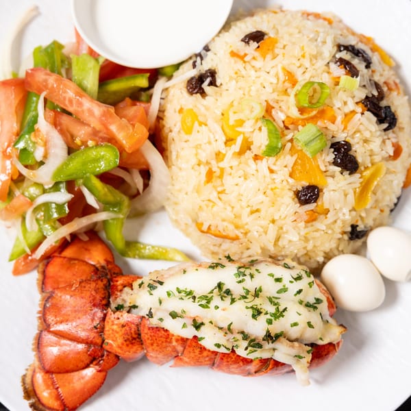 Halal lobster tail with rice pilaf, fresh salad, and two quail eggs on a white plate.