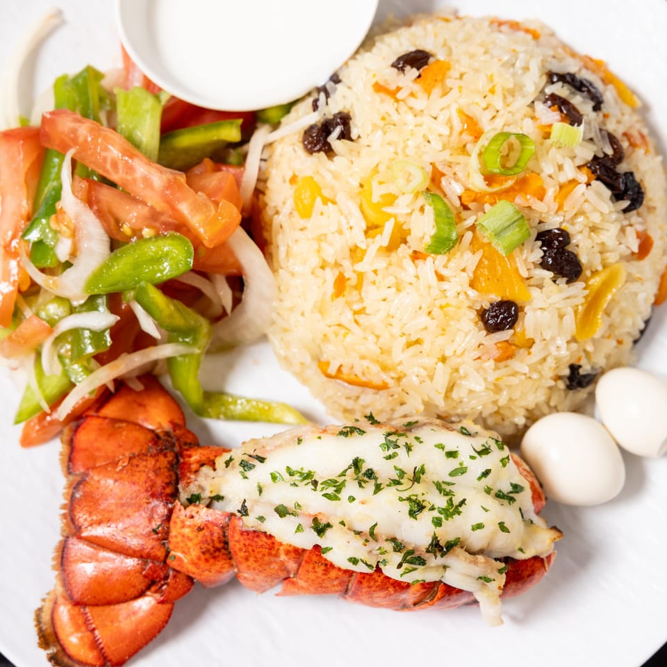 Halal lobster tail with rice pilaf, fresh salad, and two quail eggs on a white plate.
