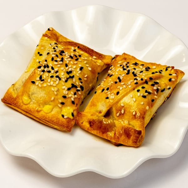 Two golden-brown Kusan Collective pastries, topped with white and black sesame seeds, on a white plate.