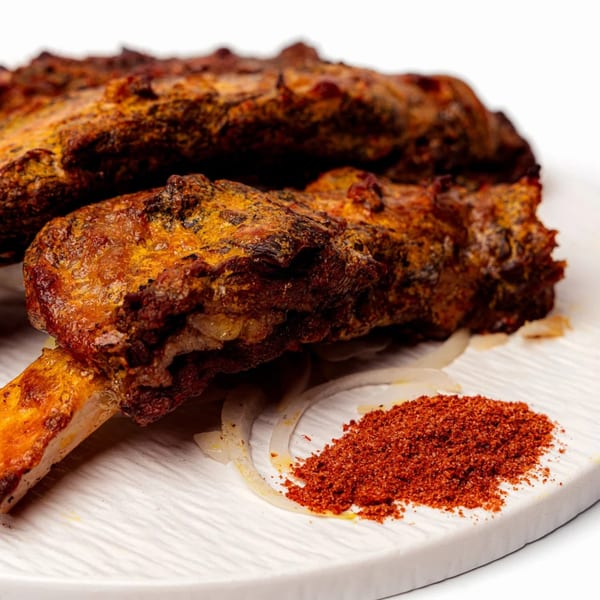 Halal lamb ribs with a golden crust, sliced onions, and a pile of red spice on a white board.